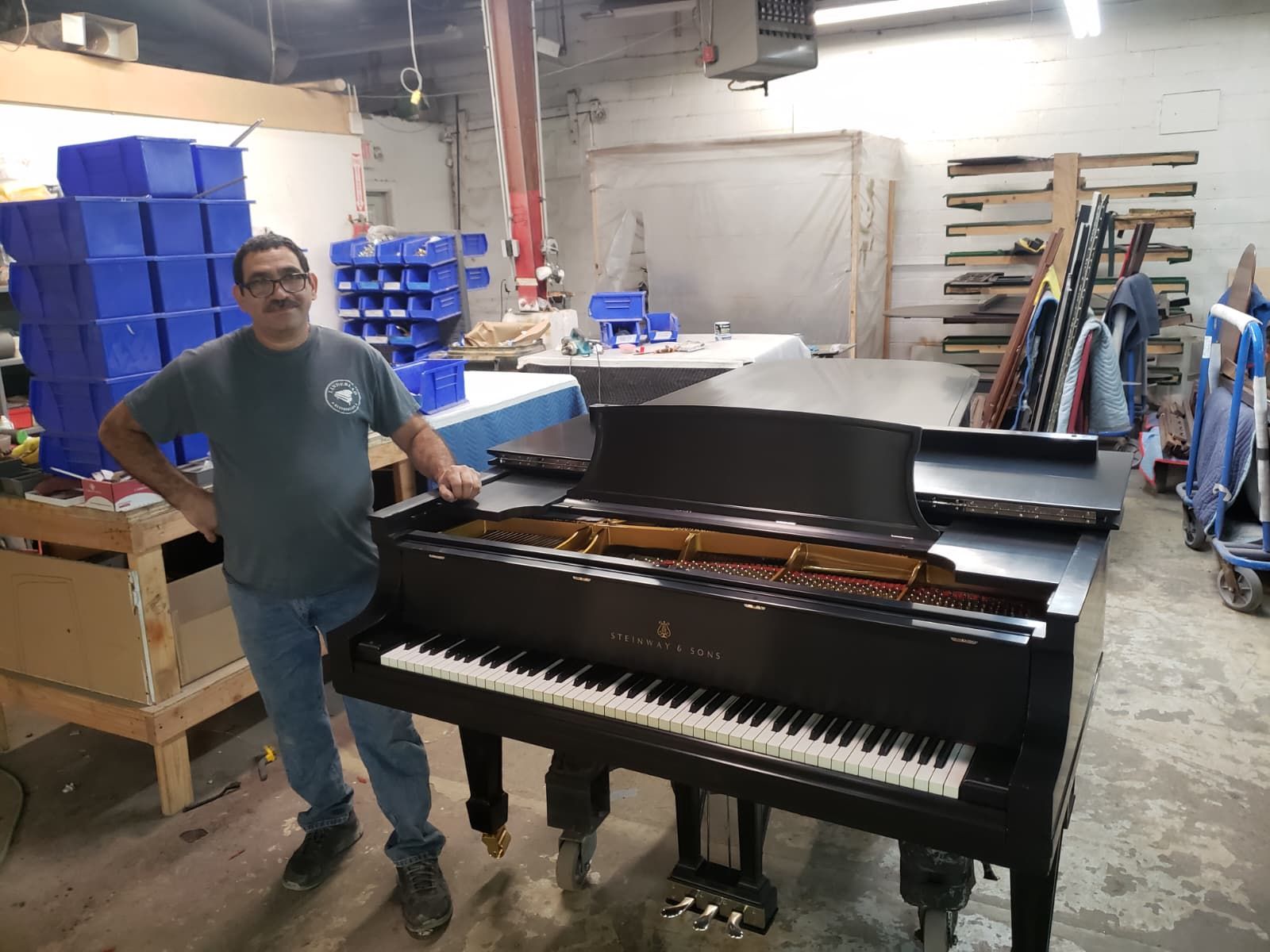 Reyman Quiros beside a restored Steinway grand piano in the JC&R workshop